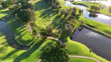 İnsansız hava aracı görüntülerinde yemyeşil, su özellikli ve uzun gölgeler bırakan manzaralı bir golf sahası görülüyor.