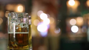 Bir bira bardağı bulanık, renkli bir arka plan karşısında duruyor, canlı ve canlı bir atmosfer yakalıyor.