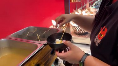 Bir satıcı Bangkok, Tayland 'da canlı bir sokak tezgahında sıcak et suyundan Kore oden şiş servis ediyor.