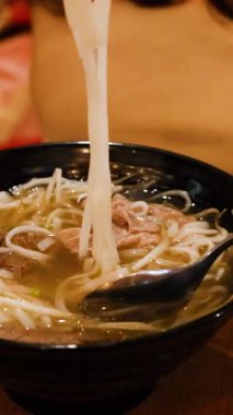 Çubuklar sıcak bir şekilde aydınlatılmış Vietnam piposu dolu bir kaseden erişte kaldırır.