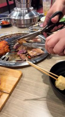 Bangkok 'ta canlı bir lokantada ızgara ızgara ızgara ızgaranın üzerinde makasla domuz eti kesen eller.