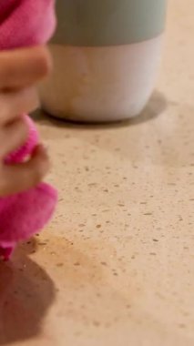 Bir el, sıcak ışığın altında mutfak tezgahında pembe bir bezle kahve dökülmesini hızla temizler.