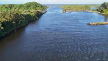 İnsansız hava aracı günbatımında yemyeşil ve sakin sularla huzurlu bir nehir manzarası yakalar.