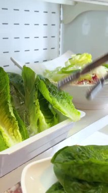 Eller sergiden taze marul yaprakları toplamak için maşa kullanır. Kore barbekü yemeğine hazırlanıyorlar.