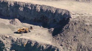 İnsansız hava aracı görüntüleri kazıcıları ve kamyonları bir taş ocağında yakalıyor, endüstriyel faaliyetleri ve engebeli araziyi gün ışığında vurguluyor.