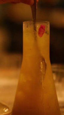 Bir barmen, sıcak ve loş ışığın altında uzun bir bardakta kokteyl karıştırır ve sıcak bir ortam yaratır.