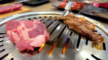 Bangkok 'taki Kore mangalında et ızgarası. Canlı renkler, dinamik kamera açıları ve cızırtılı hareketler mutfak deneyimini yakalar.