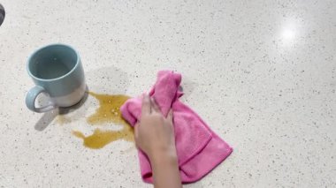 Bir insan parlak ışığın altında açık bir tezgahın üzerine pembe bir bezle kahve döker.