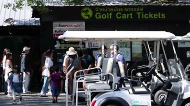 İnsanlar golf arabası bilet alanının yakınında toplanıyor.