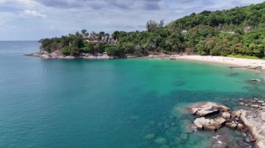 Drone görüntüleri Phuket 'in canlı sahil şeridini çekiyor, turkuaz sular, yemyeşil yemyeşil ve açık gökyüzünün altında kumlu plajlar sergiliyor.