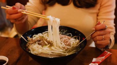 Bir insan yemek çubuklarını ustalıkla sıcak bir restoranda buharlı bir kase Vietnam piposu yemek için kullanır.