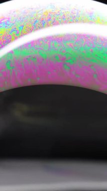 Bir sabun köpüğü yüzeyinde canlı renkler kıvrılır ve yakın çekim görüntüsünde dinamik desenler yaratır.