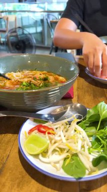 Parlak bir Bangkok restoranında taze bitkiler ve sebzelerle bir kase Vietnam piposunun tadını çıkarıyor.