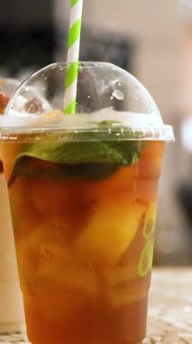 Bir el, temiz bir fincanda nane yapraklarıyla buzlu çayı karıştırır. Parlak ışıklandırma canlandırıcı ortamı güçlendirir