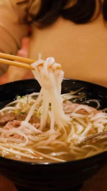 Buharda pişen bir kase Vietnamlı piposundan sıcak yemek çubuklarını ustalıkla kaldıran bir insan.