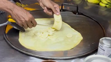 A street vendor skillfully prepares banana roti on a hot griddle in Phuket, showcasing traditional Thai street food techniques
