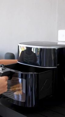 A person operates an air fryer, adjusting settings and checking food in a sleek, modern kitchen environment