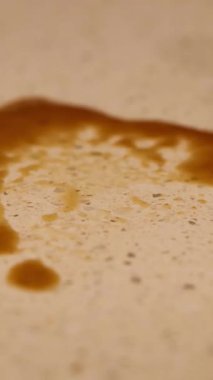A coffee spill is cleaned with a yellow cloth on a speckled countertop in warm lighting