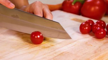 A hand slices cherry tomatoes with a knife