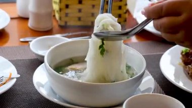 Person eating noodle soup at a dining table