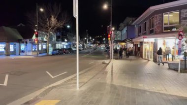 A bustling Queenstown street at night, illuminated by streetlights and shop windows, capturing a lively urban atmosphere