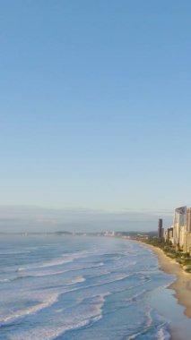 Aerial footage of Gold Coast's coastline with waves, skyscrapers, and clear skies. Captures serene beach atmosphere and urban landscape