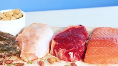 A vibrant display of various protein foods including meats, seafood, and nuts against a blue background