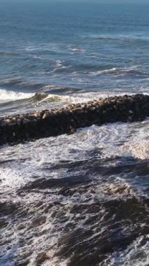 Dynamic ocean waves crash against a rocky breakwater under clear skies at Brunswick Heads, NSW, Australia
