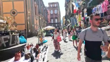 İnsanlar canlı bir pazarda alışveriş yapıp yürüyorlar.