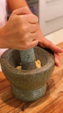 Elleri, iyi aydınlatılmış bir mutfakta ahşap bir yüzeye malzeme öğütmek için havan ve tokmak kullanıyor.