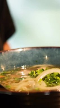 Bir Bangkok restoranındaki dumanı tüten bir kase çorbadan erişte aşıran yemek çubuklarının yakın çekimi. Canlı malzemeler ve dokular.