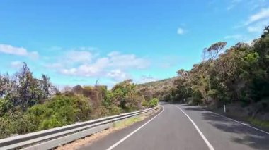 45 saniyelik bir video, dolambaçlı Büyük Okyanus Yolu boyunca, yemyeşil ve açık mavi gökyüzünü gösteren bir sürüş yakalıyor.