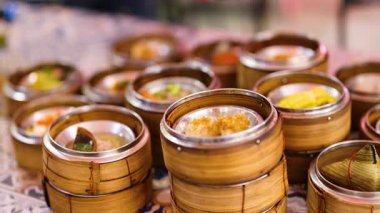 Hands choose dim sum from bamboo steamers in a vibrant market. Warm lighting enhances the lively, bustling atmosphere