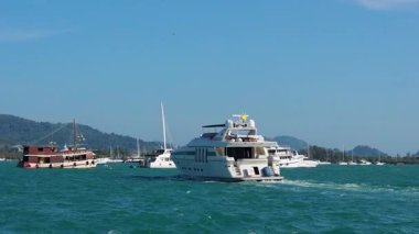 Motor yachts and fishing boats traverse the turquoise ocean near Ko Racha Yai, under clear skies in Phuket, Thailand