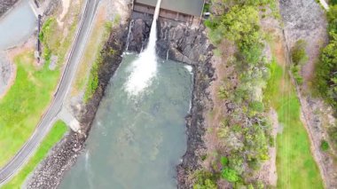 Su, yemyeşil sularla çevrili barajın üzerinden akıyor.