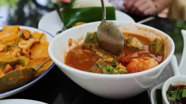 Hands serving sour tamarind soup into plates