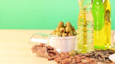 Ahşap bir masada yeşil bir zemine karşı sıralanmış çeşitli yağlar ve fındıklar sağlıklı yiyecek seçenekleri sunuyor.