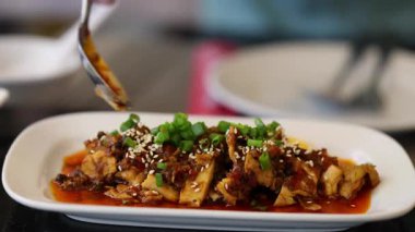 Bir el, susam tohumlarıyla süslenmiş baharatlı Asya tavuğu ve canlı bir tabakta yeşil soğan servis eder.