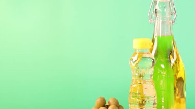 Yağ şişeleri, fındık kaseleri ve tohumlar yeşil arka planlı ahşap bir masanın üzerinde. Parlak ışıklandırma renkleri güçlendirir