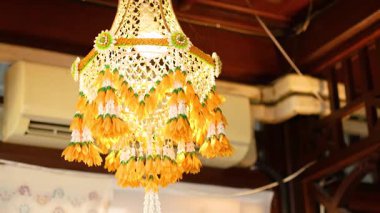 Canlı bir Tayland çiçek arabası kapalı mekanda asılı, sıcak bir şekilde aydınlatılıyor. Karmaşık tasarım ve parlak renkler neşeli bir atmosfer yaratır.