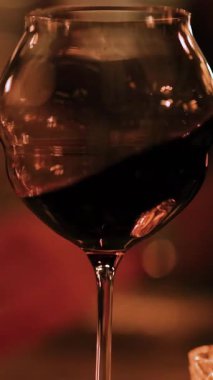 A wine glass is gently swirled, showcasing rich red wine under warm, ambient lighting in a sophisticated setting