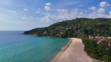 Drone footage captures a serene Phuket beach with lush greenery and turquoise waters under a clear sky