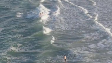 Drone captures surfers navigating waves at Gold Coast beach. Dynamic movement, natural lighting, and oceanic scenery create an exhilarating atmosphere