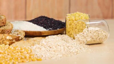 A variety of grains, pasta, and bread arranged on a wooden table with natural lighting