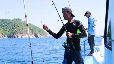 Phuket, Tayland 'da bir teknede balık tutan iki kişi, gün ışığında dingin okyanus manzaraları ve odaklanmış aktiviteler sergiliyorlar.