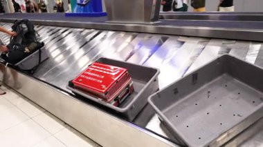 Bangkok, Tayland 'da bir havaalanı taşıma bandı boyunca parlak ışık altında kırmızı bir bavul hareket eder ve tipik bir seyahat sahnesini yakalar.