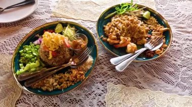 Dantel bir masa örtüsü üzerinde karides ve sebzeli renkli bir Tayland yemeği, yukarıdan aşağı manzaralı doğal ışıkla yakalanmış.