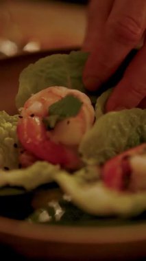 Bir el nazikçe karides birleştirir marul yaprakları üzerinde, sıcak, yumuşak bir aydınlatma altında, rahat bir ortamda.