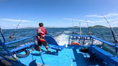 Canlı mavi bir teknede, Phuket, Tayland 'ın berrak sularında, berrak gökyüzünün altında balık tutan bir adam.