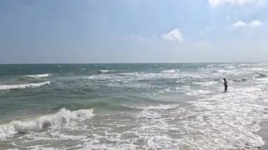 Okyanus dalgalarında duran kişi, gökyüzünde bulutlar